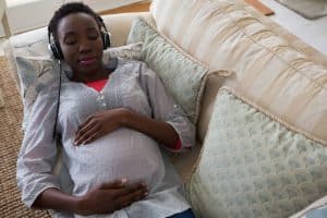 Pregnant woman lying on sofa listening to hypnosis on headphones at home