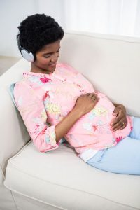 Pregnant person laying on couch with headphones on