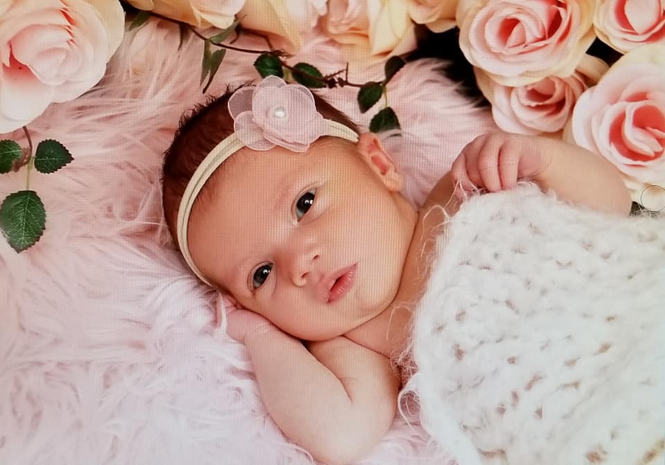 Hypno-mom Jamie's newborn baby with a flower headband on looking at the camera and surrounded by roses