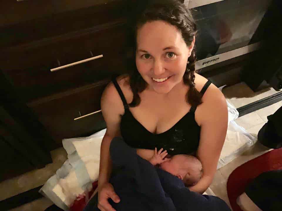 Hypno-mom Audree on the floor holding newborn daughter smiling.