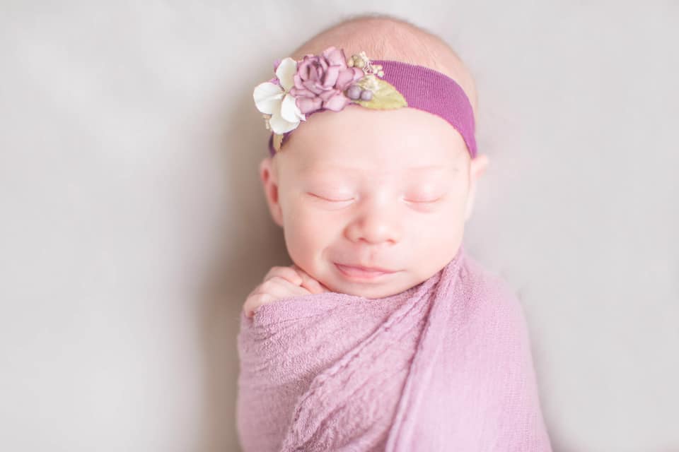 Hypno-mom Brooke's newborn baby wrapped in pink blanket with flowered headband.