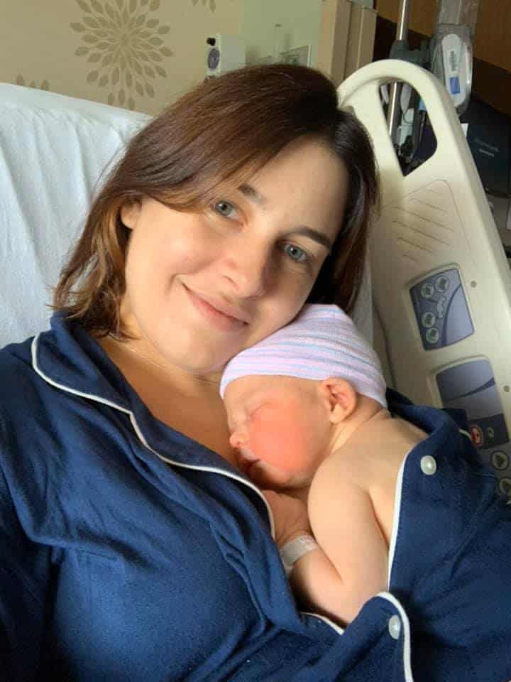 Hypno-mom Laura smiling with her newborn baby tucked inside her blue Pajama top.