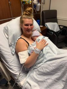 Hypno-mom Emily in hospital bed holding newborn and smiling