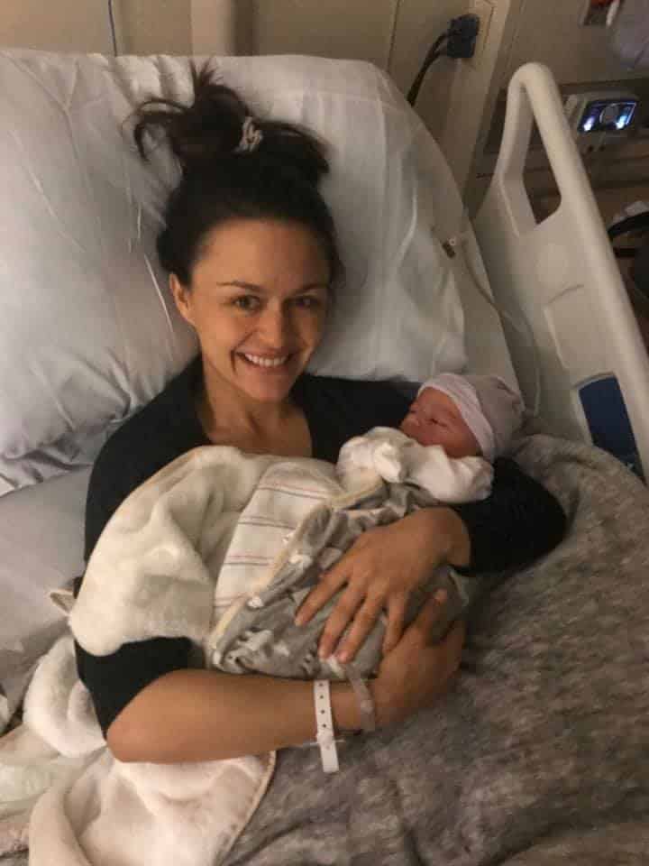 Hypno-mom Tahnee sitting up in hospital bed smiling and holding newborn baby.