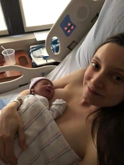 Hypno mom holding newborn baby and smiling at the camera.