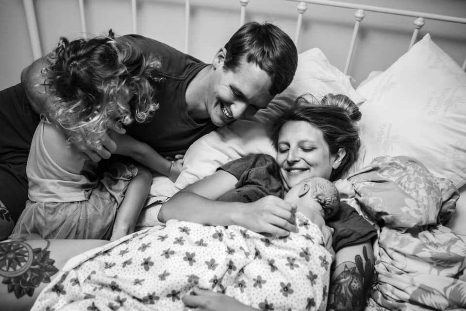 hypno-family laying in bed smiling and cuddling their newborn