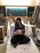 Hypno-mom sitting in hospital bed holding newborn with fist in the air