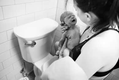 Hypno-mom holding newborn after giving birth on toilet.