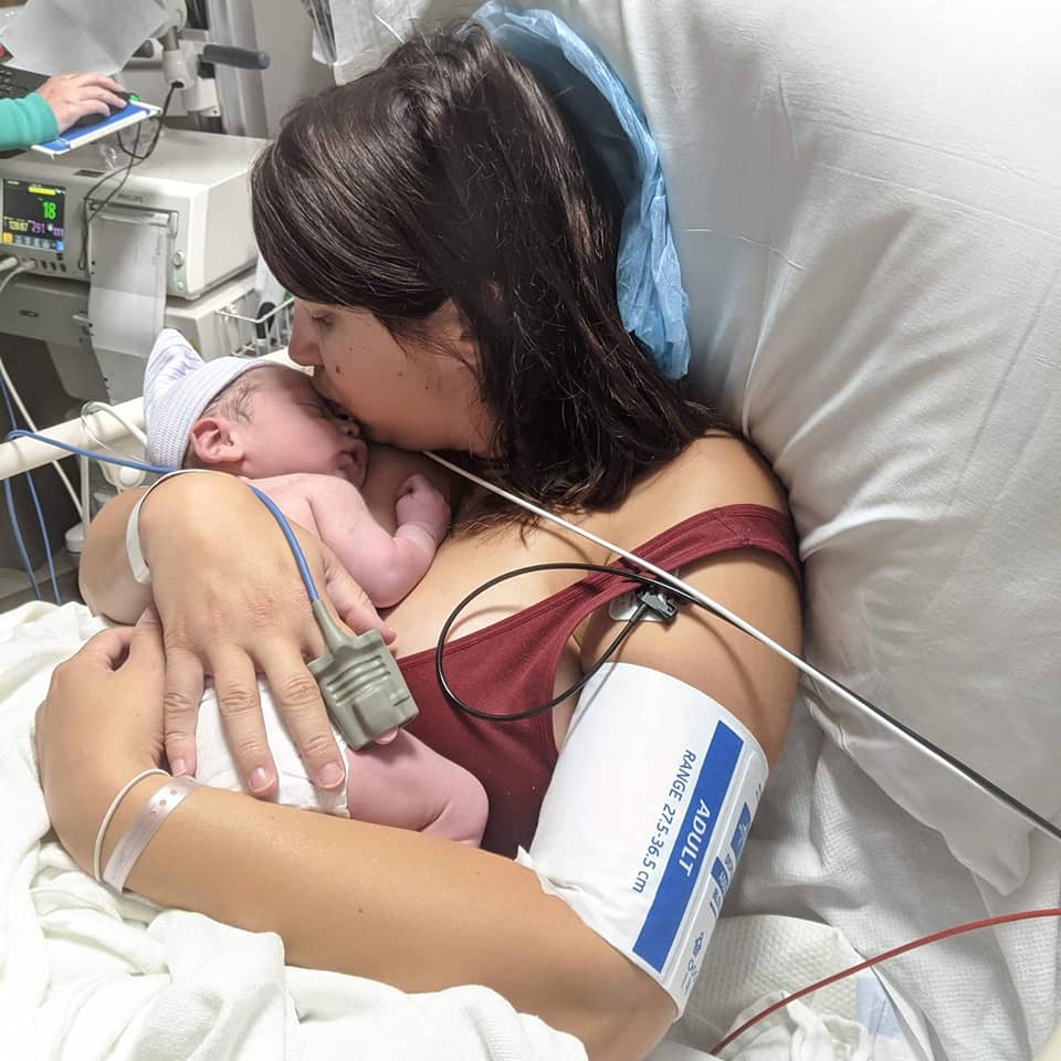 Hypno mom in hospital bed holding and kissing newborn and wearing a blood pressure cuff and pulse oximeter