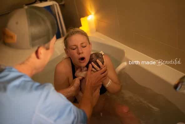 Birth partner passing newborn baby to hypno-mom who has a look of amazement on her face.