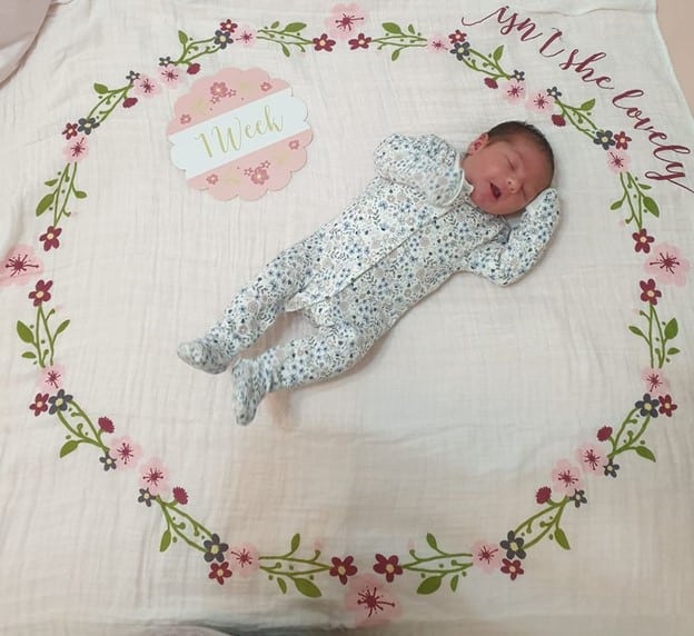 Newborn baby laying on a blanket with a sign saying 1 week