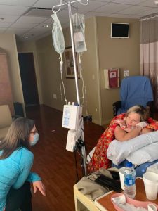 Birthing person leaning over hospital bed hooked up to iv and talking with doula
