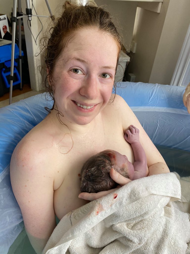 new parent just after giving birth sitting in the birth tub smiling and holding newborn