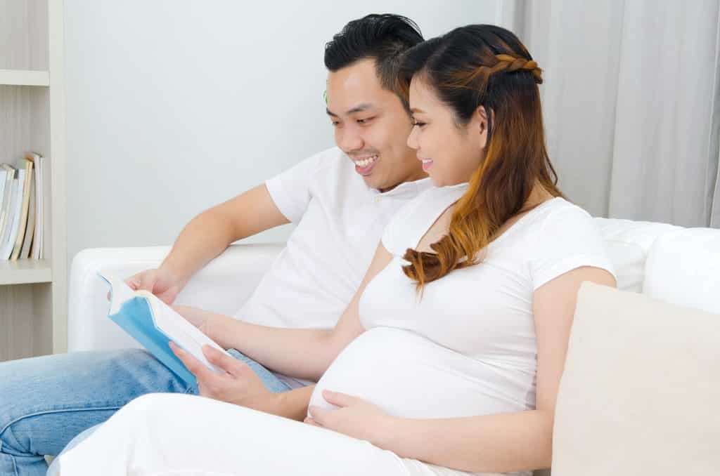 pregnant student and partner sitting on sofa and reading book. Benefits of Hypnobabies Self Study