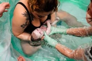 New parent in birth tub pulling up newborn just after birth