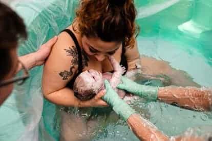 New parent in birth tub pulling up newborn just after birth
