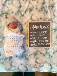 swaddled newborn laying next to a sign with birth statistics 