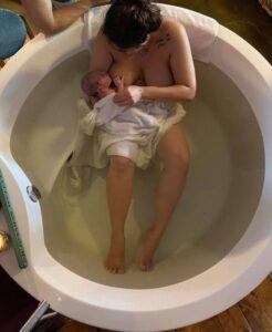 birthing person in birth tub holding new baby