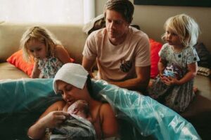 birthing person holding newborn in birth tub with family watching