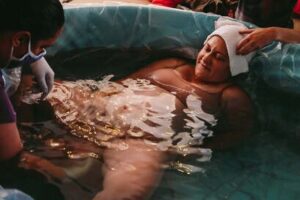 birthing person in birth tub pushing with support of midwife during magical home birth