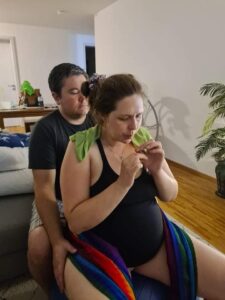 birthing person on birth ball eating honey stick with partner supporting from behind