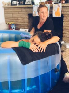 birthing person leaning over side of tub with midwife in the background