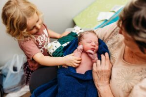 Grandma and new baby with older grandchild helping