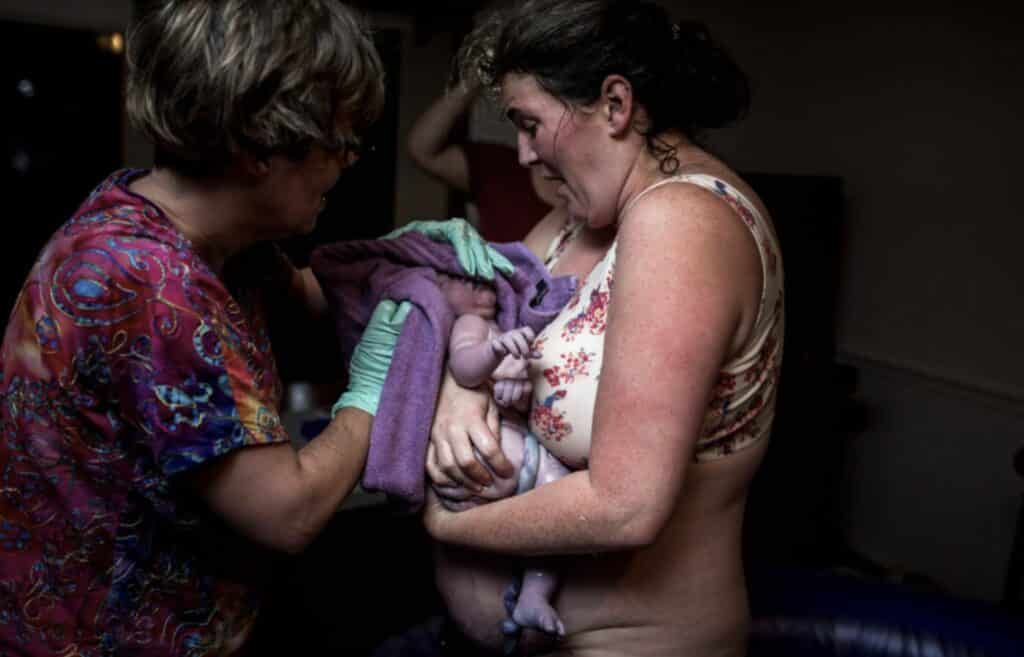 birthing person just after birth kneeling in birth pool and holding newborn