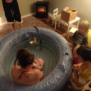 new parent in tub with newborn and other children watching