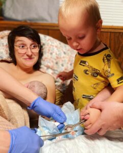 sibling helping cut newborn baby's umbilical cord