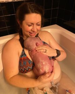 New parent in tub holding brand new baby just after birth