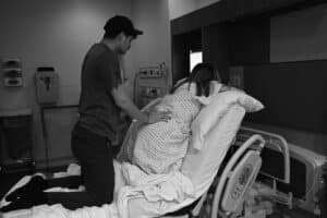 pregnant person and partner kneeling on hospital bed