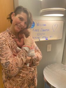 New parent holding newborn and smiling in front of sign announcing newborn name