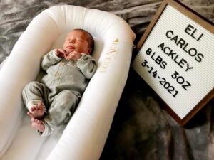 New born baby in a bassinet wearing a sleeper with a sign announcing name, weight and birth date