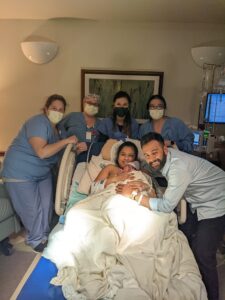 New parents with newborn baby surrounding by hospital birth team wearing masks