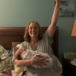 New parent holding newborn baby raising arm in triumph