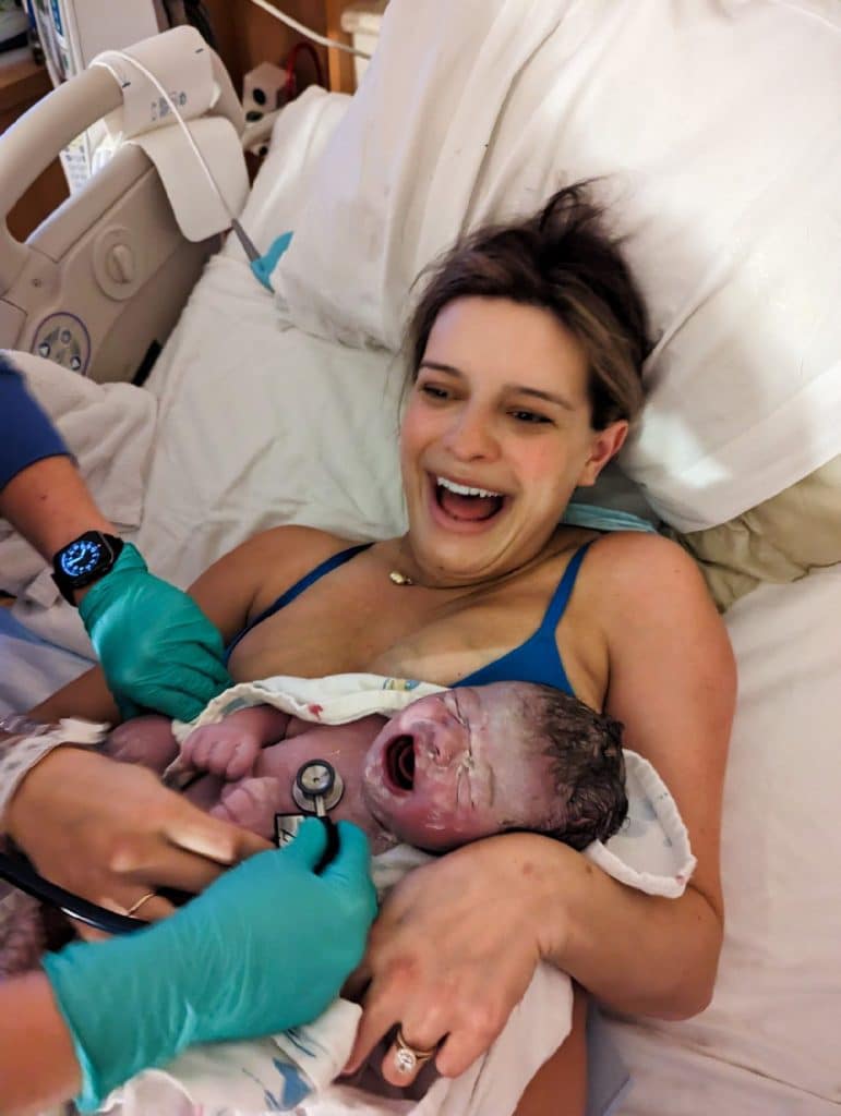 Hypnobabies mom just after her peaceful birth holding her newborn while care provider checks heart rate