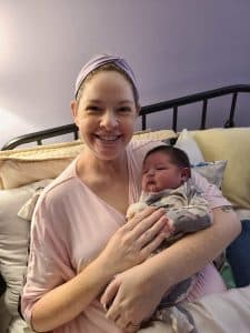 New parent sitting in bed holding newborn baby and smiling
