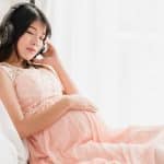 Pregnant woman sitting on the bed listen to music in headphones for easier birth