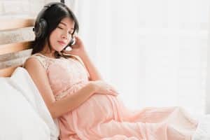 Pregnant woman sitting on the bed listen to music in headphones