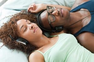 Man and woman listening to hypnosis with headphones, lying down, eyes closed