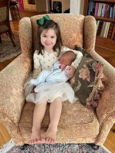 Big sister sitting in a chair holding her new sibling after calm focused Hypnobabies birth