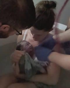 New parent in birth tub holding newborn