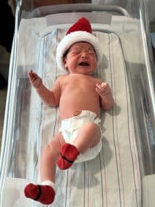 Newborn baby in bassinet wearing a santa hat and booties