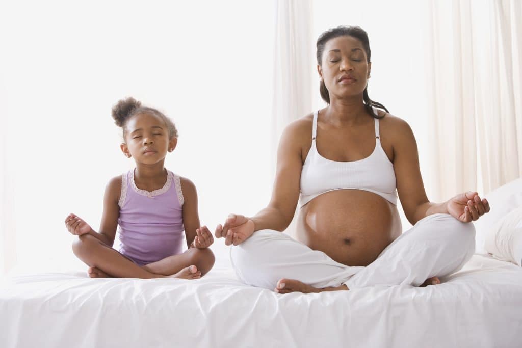 Pregnant mother with daughter sitting on the bed meditating