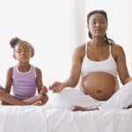 Pregnant mother with daughter sitting on the bed meditating